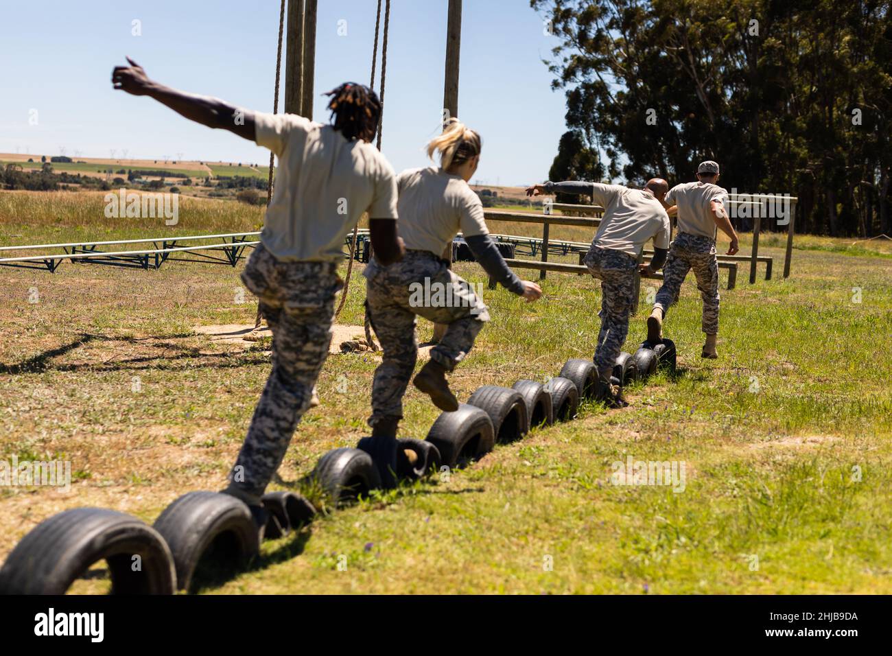 Group of male and female diverse soldiers walking on tires during obstacle course at boot camp Stock Photo