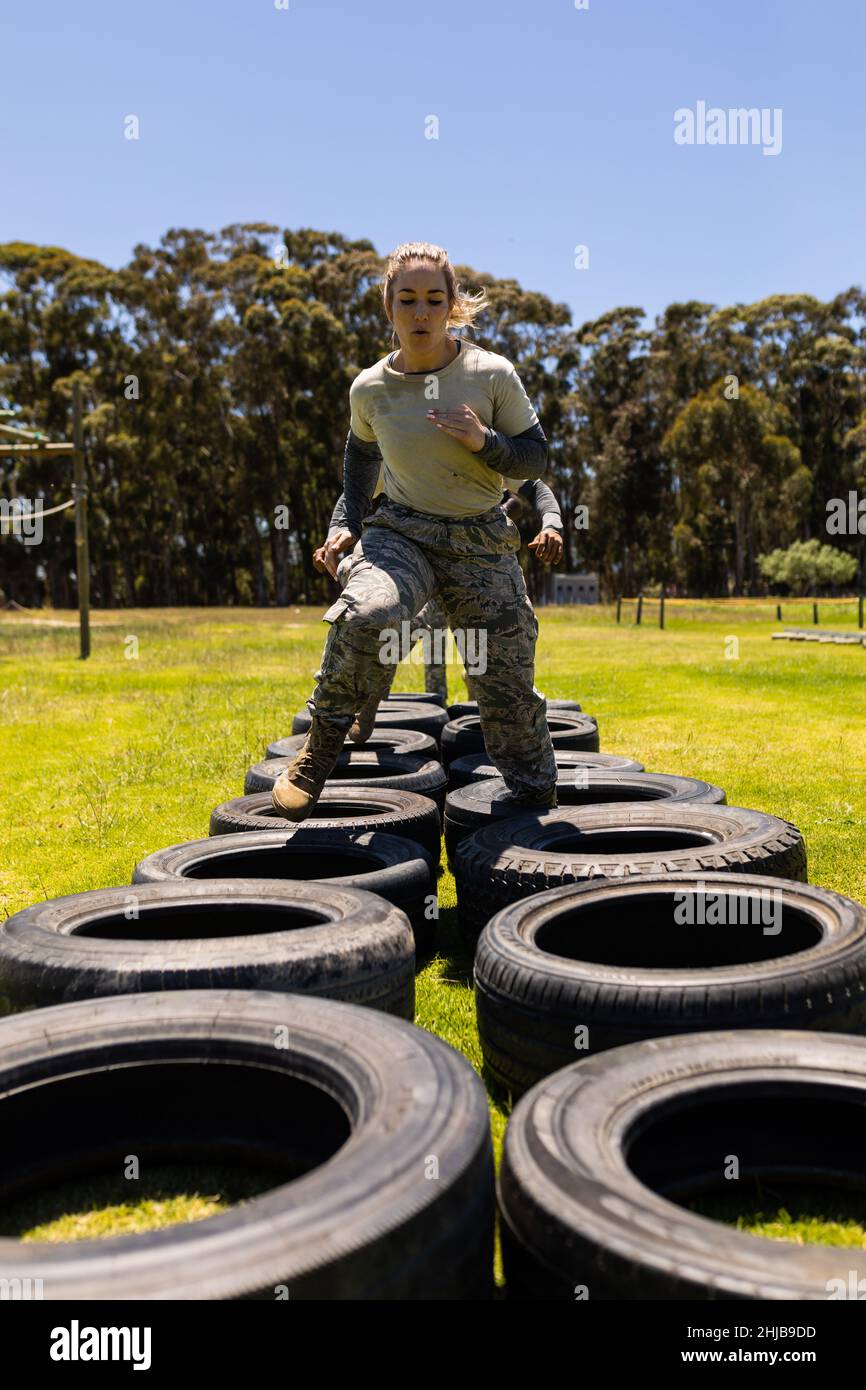 Caucasian female soldier running on tires during obstacle course at boot camp Stock Photo