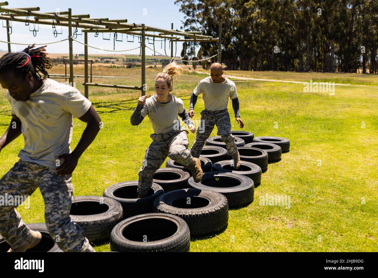 Group of diverse male and female soldiers running on tires during obstacle course at boot camp Stock Photo
