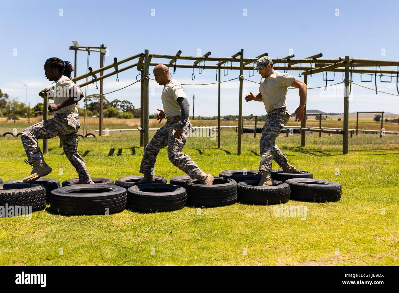 Three diverse male soldiers running on tires during obstacle course at boot camp Stock Photo