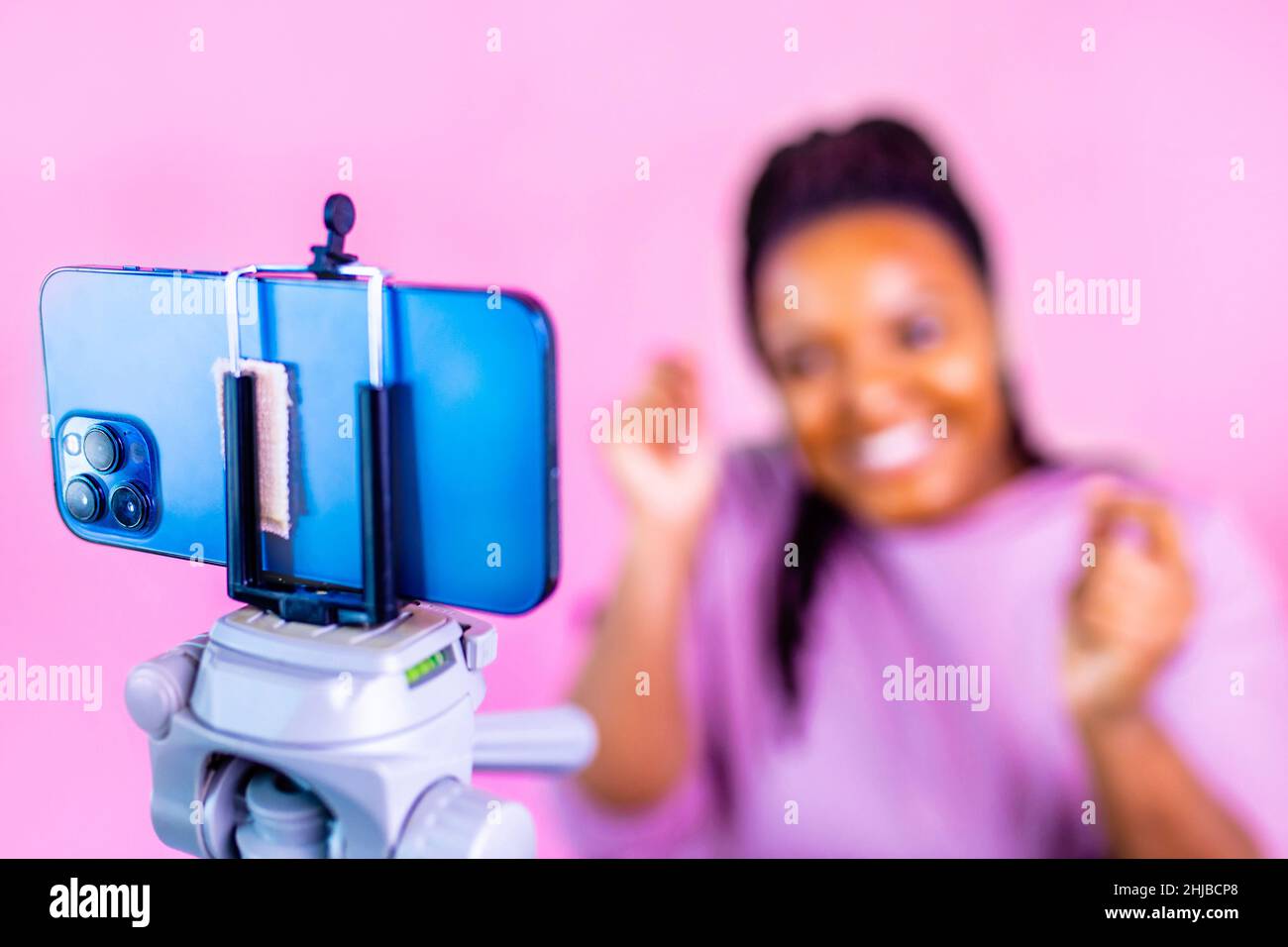 hispanic woman with cool dreadlocks pigtails wear pink dress in studio chatting with her subscribers by phone camera Stock Photo