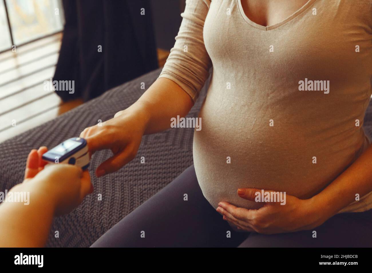 Pregnant woman with pulse oximeter on finger. Doctor measuring oxygen saturation level while visiting expectant mother with coronavirus disease at hom Stock Photo