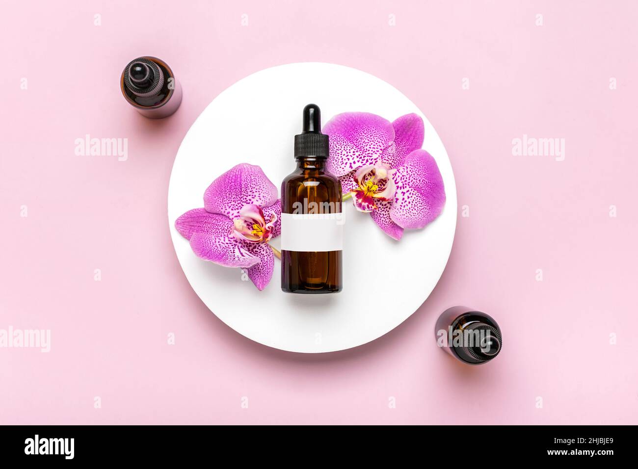 glass cosmetic bottle with moisturizing natural oil, Orchid lie on white podium isolated on pink background Top view Flat lay Eco, bio, zero waste Stock Photo