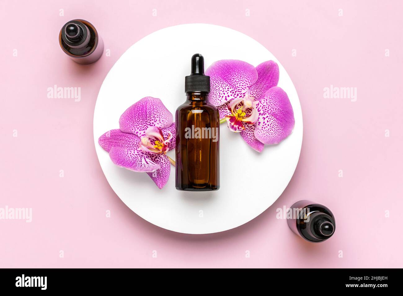 glass cosmetic bottle with moisturizing natural oil, Orchid lie on white podium isolated on pink background Top view Flat lay Eco, bio, zero waste Stock Photo