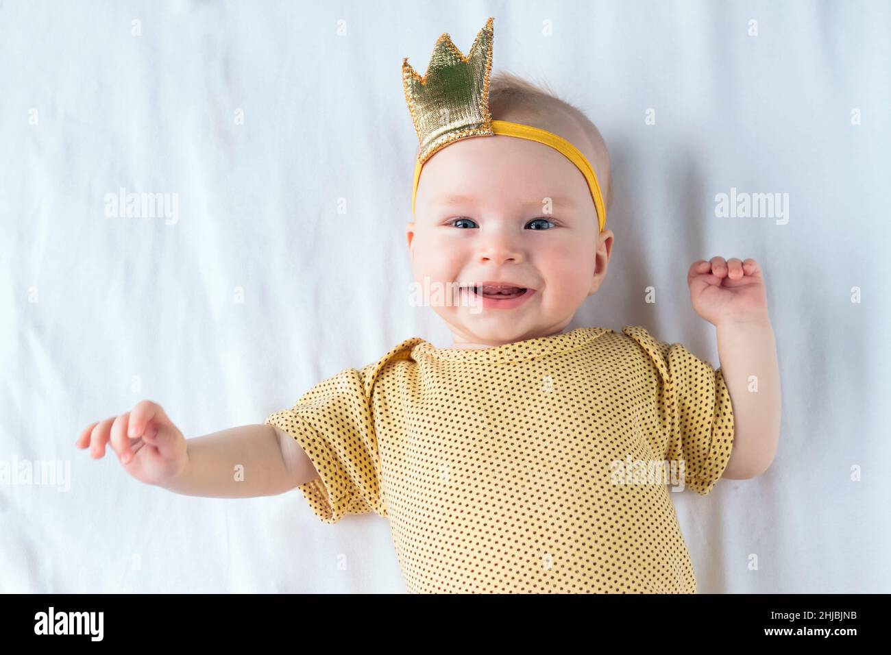 Portrait of happy 4-months-old baby girl lying on the white sheet in bed at home Stock Photo