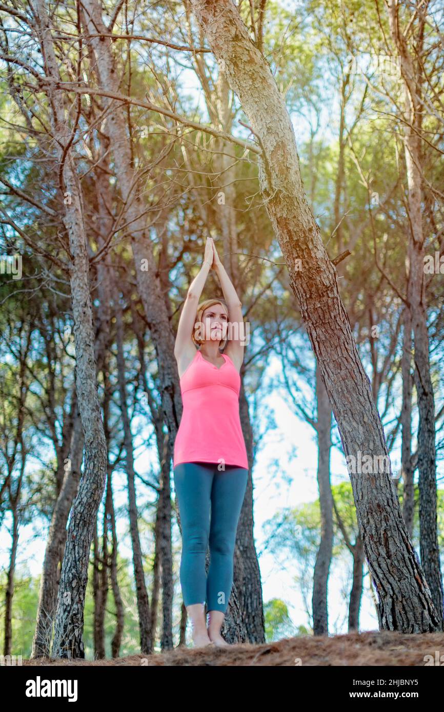 Happy young woman practicing yoga with hands raised up into the woods outdoors. Upward Salute pose Stock Photo
