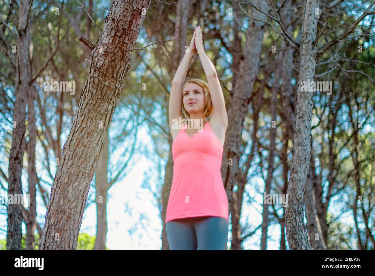 Happy young woman practicing yoga with hands raised up into the woods outdoors. Upward Salute pose Stock Photo