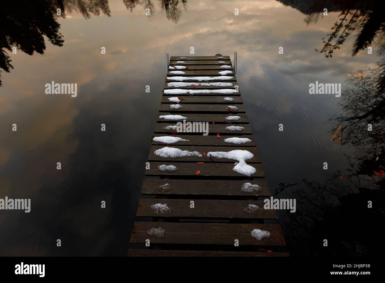 snow covered wooden pier on peaceful lake reflecting the evening sky Stock Photo