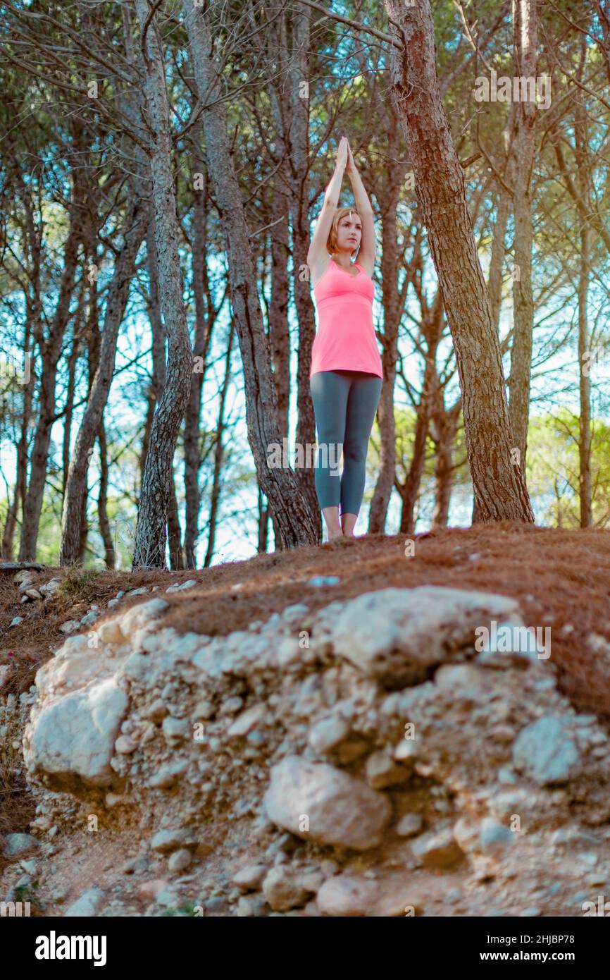 Serious young woman practicing yoga with hands raised up in a forest or park outdoor with trees on the background Stock Photo