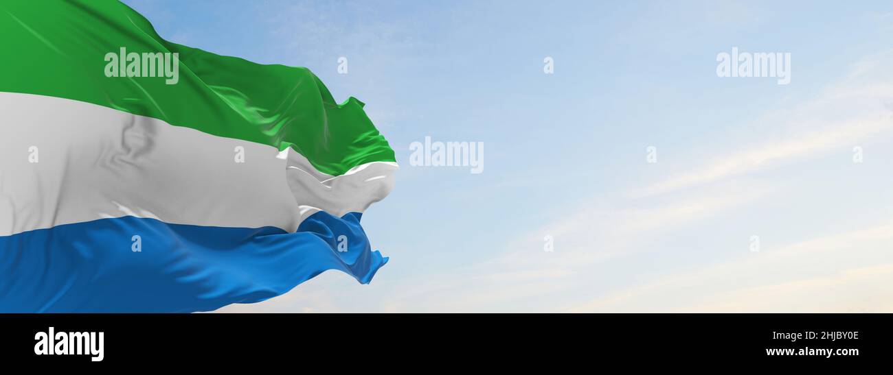 official flag of Sierra Leone at cloudy sky background on sunset ...