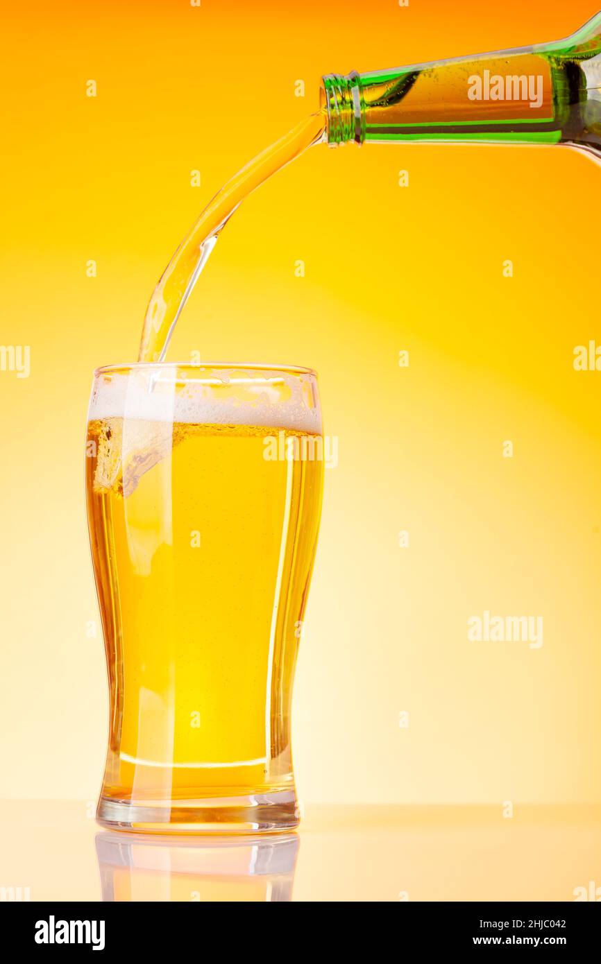 Beer pouring from bottle into glass in front of yellow background. Studio shot with copy space