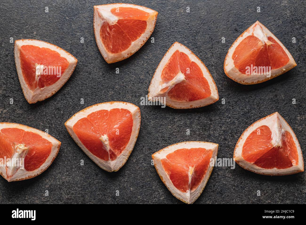 Sliced citrus fruit. Chopped fresh grapefruit on a black table. Top view. Stock Photo