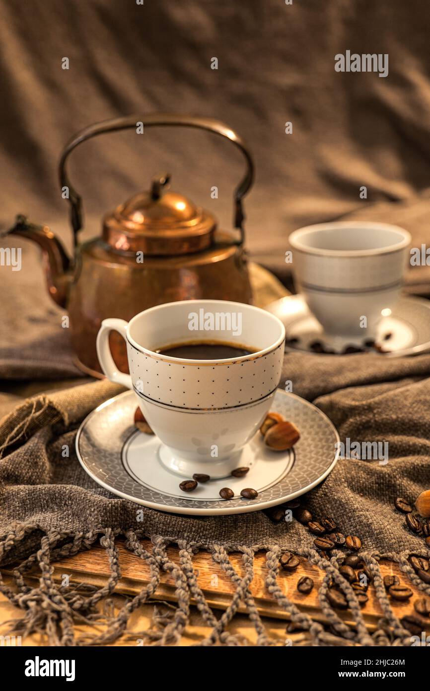 Two cups of coffee, a copper teapot in the background, shades of brown and gray, fabric in shades of gray Stock Photo
