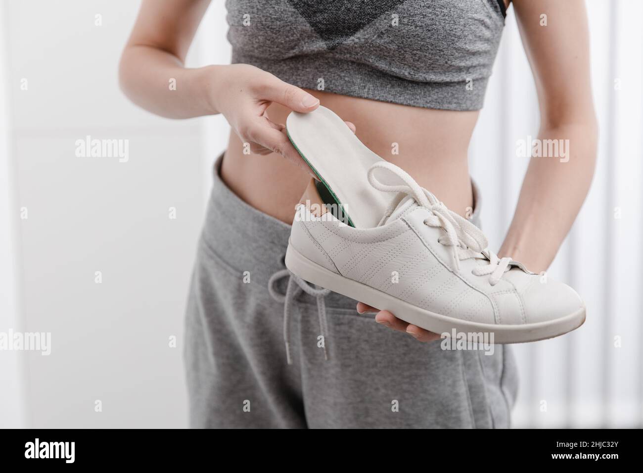 Woman putting orthopedic insole into shoe at home. Sports girl fitting orthopedic insole indoors, close up. Foot care banner. Flat Feet Correction Stock Photo