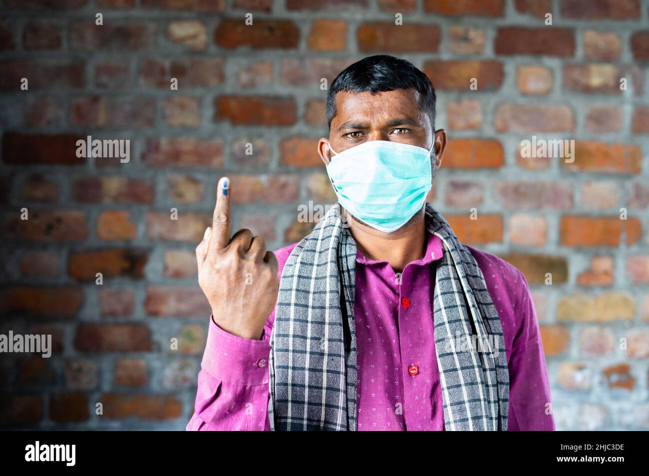 Construction worker with medical face mask showing ink marked finger after voting in election by looking camera - concept of democracy and Indian poll Stock Photo