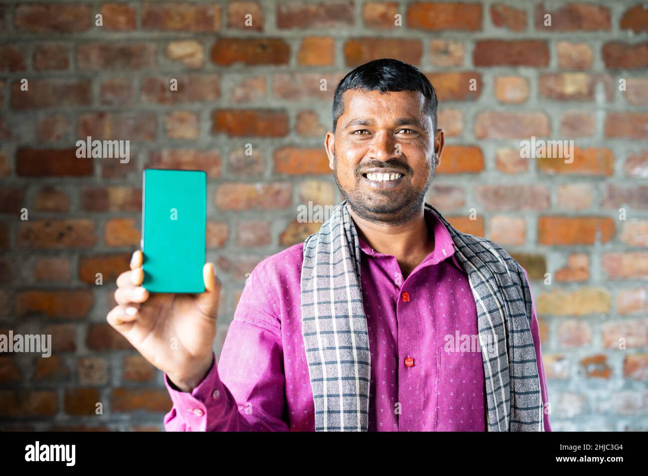 rack focus shot of indian daily wager showing green screen mobile phone by looking at camera - concept of technology, blue collar job, advertisment Stock Photo