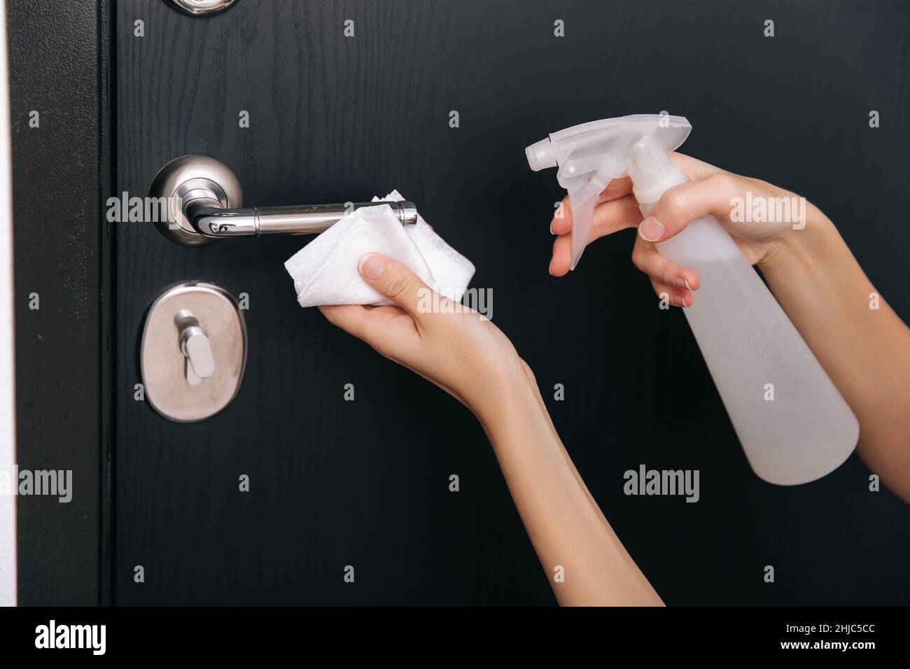 Cleaning black door handles with an antiseptic wet wipe and sanitizer spray. Disinfection in hospital and public spaces against corona virus. Woman Stock Photo