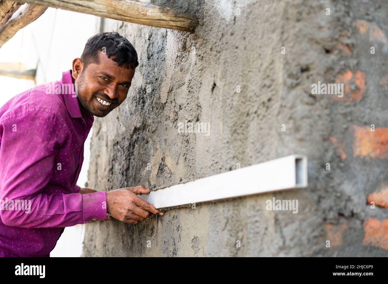 Happy smiling construction labor leveling wall plastering using wooden tool at workplace - concept of hard working, skilled manual labour and daily Stock Photo