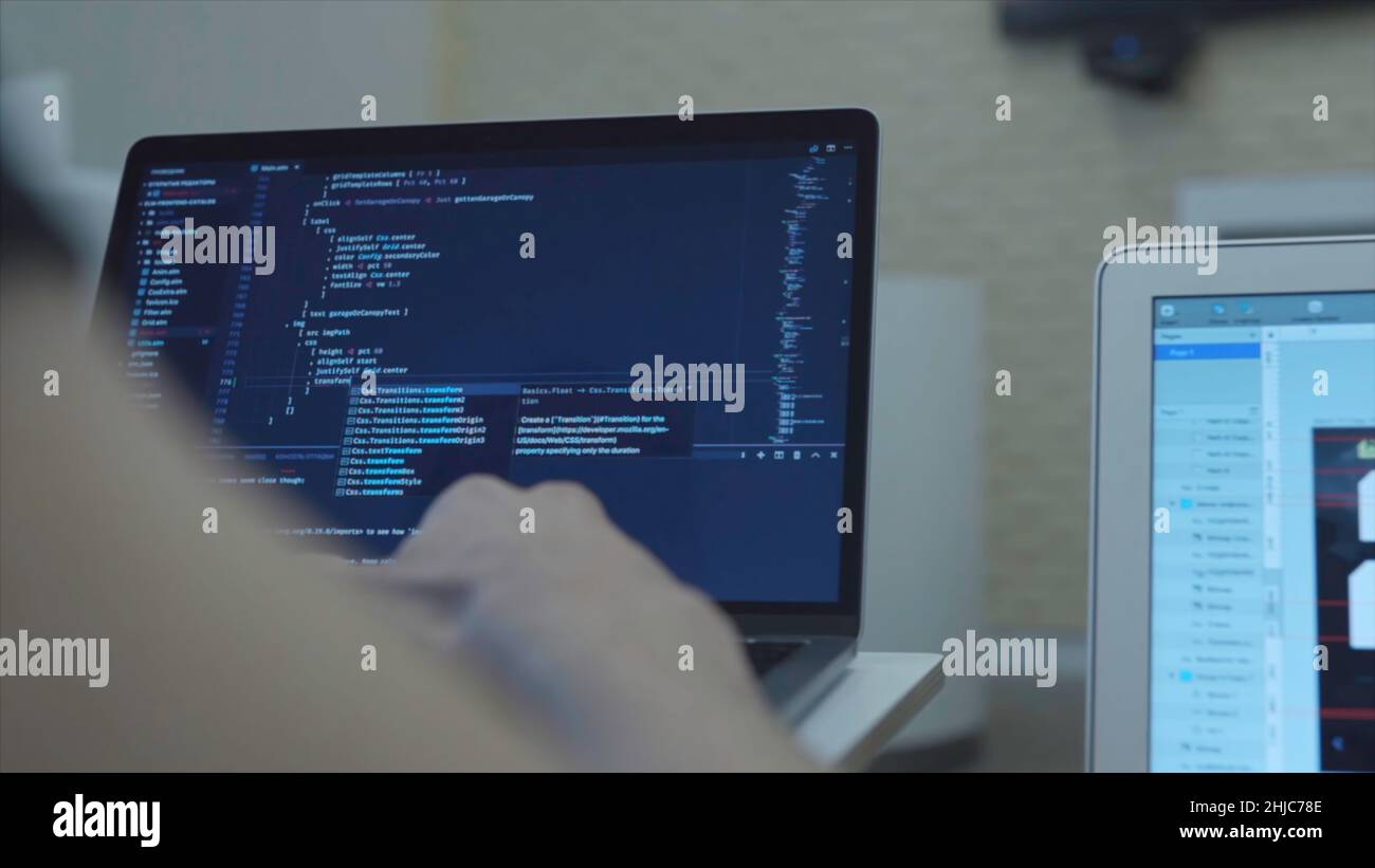 Close-up of web developer's hands programming Javascript, coding HTML on laptop. View from back Stock Photo