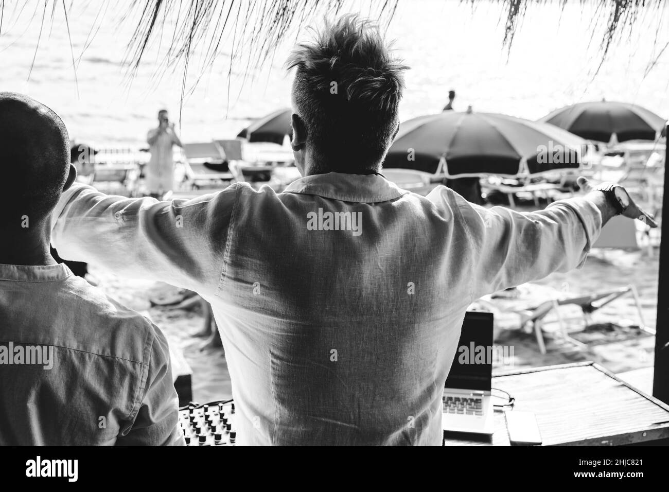 Back view of disc jockeys playing music for tourist people at club party outdoors on the beach - Djs at music live event - Music and fun concept - Ent Stock Photo