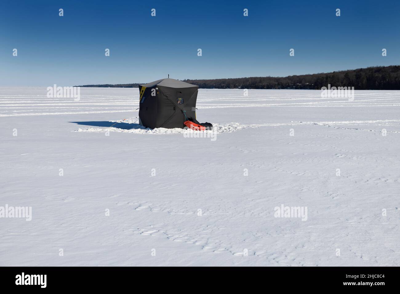 Black ice fishing hut on frozen snowy Kempenfelt Bay of Lake Simcoe in winter Barrie Ontario Canada with blue sky Stock Photo