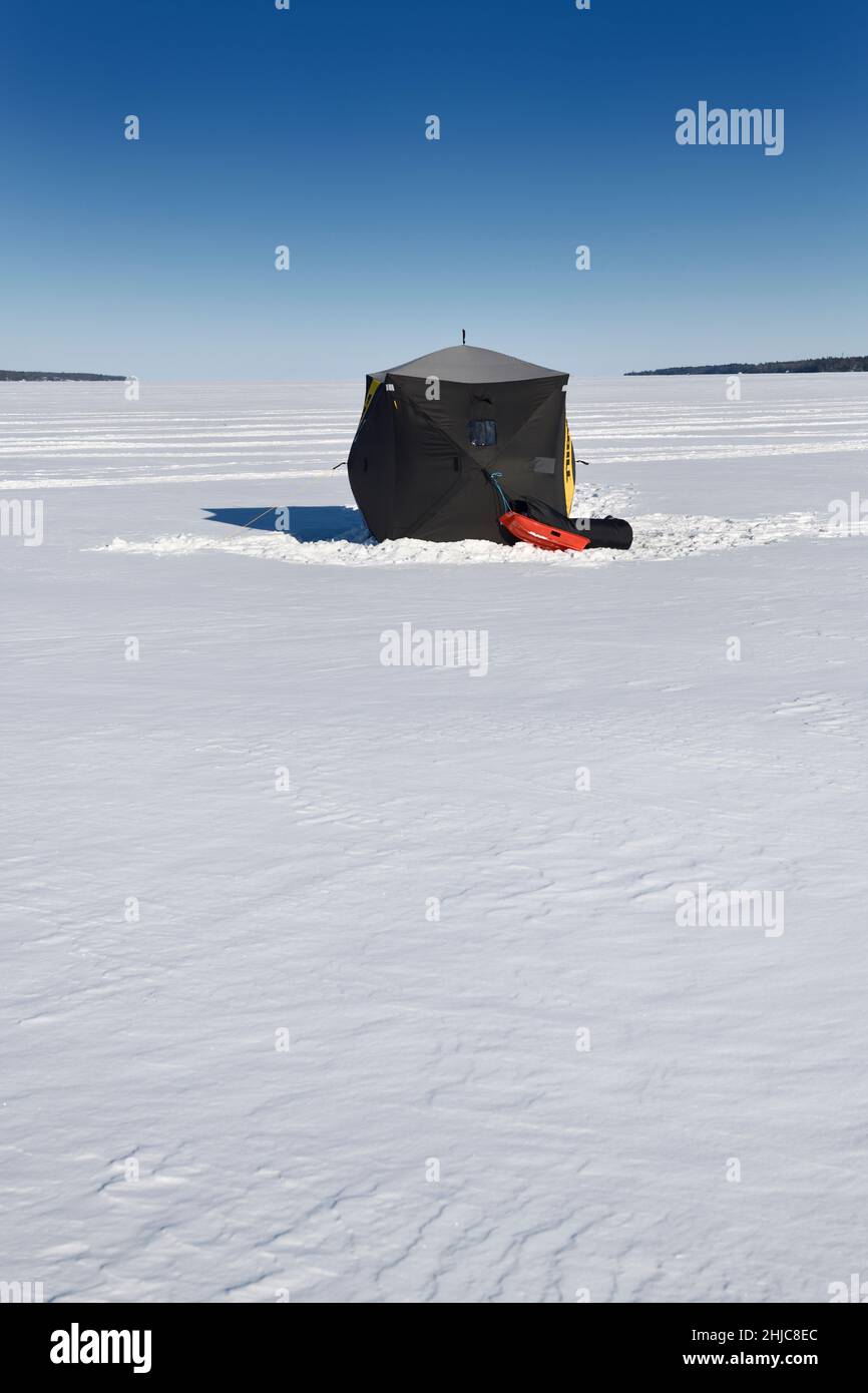 Black ice fishing hut in snow on frozen Kempenfelt Bay of Lake Simcoe in winter Barrie Ontario Canada with blue sky Stock Photo