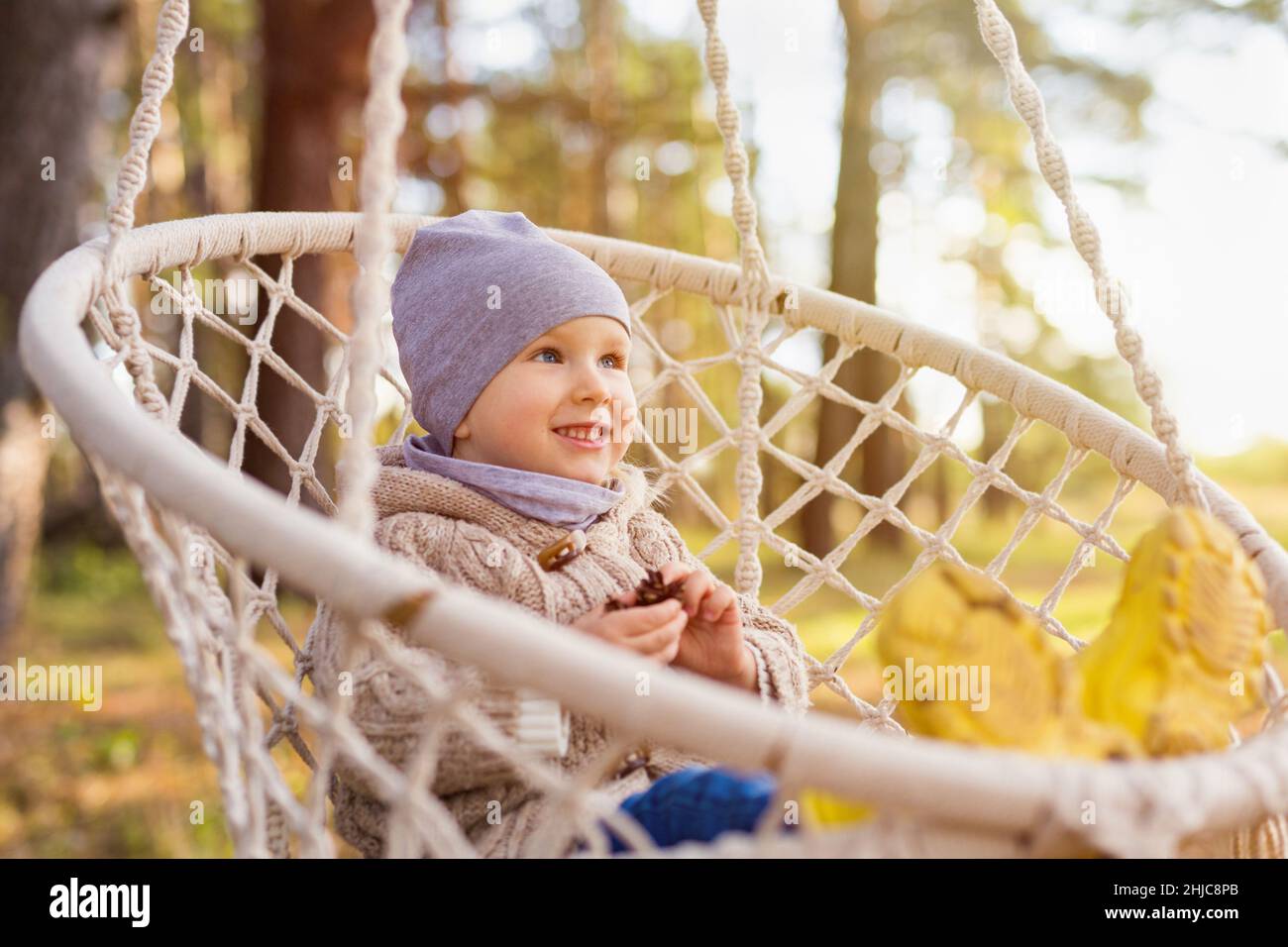 Portrait of happy 3-years-old toddler sitting in a hanging chair or hammock in a forest Stock Photo