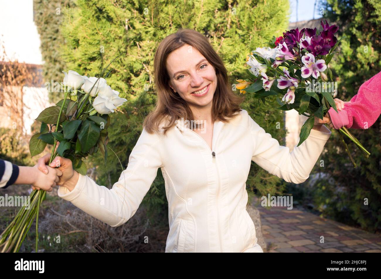 portrait of a happy smiling woman, to whom children's hands hold out two bouquets of flowers. Joyful emotions, positive, motherhood. Congratulations f Stock Photo
