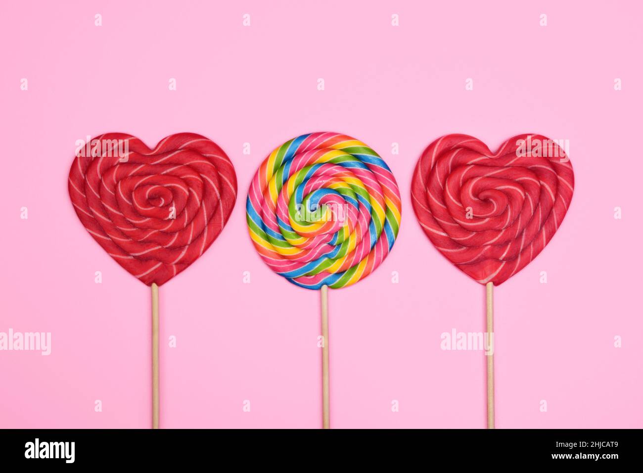Two large red heart-shaped lollipops and a round multicolor lollipop on