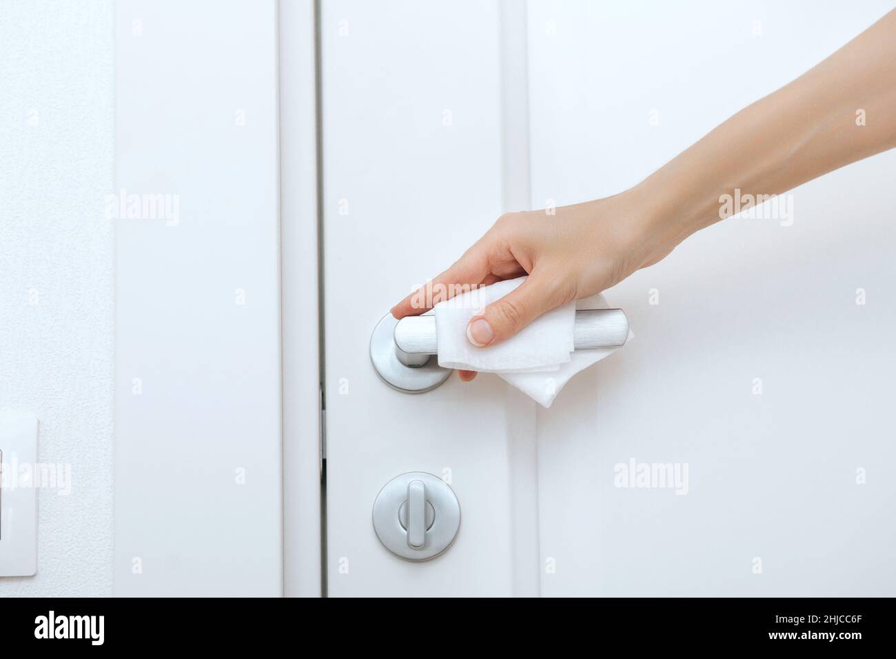 Cleaning door handles with an antiseptic wet wipe and gloves. Sanitize surfaces prevention in hospital and public spaces against corona virus. Woman Stock Photo