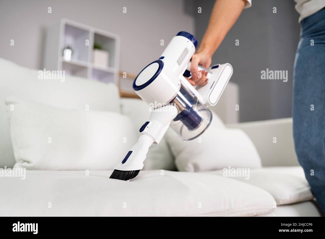 Young Female Worker Cleaning Sofa With Vacuum Cleaner Stock Photo