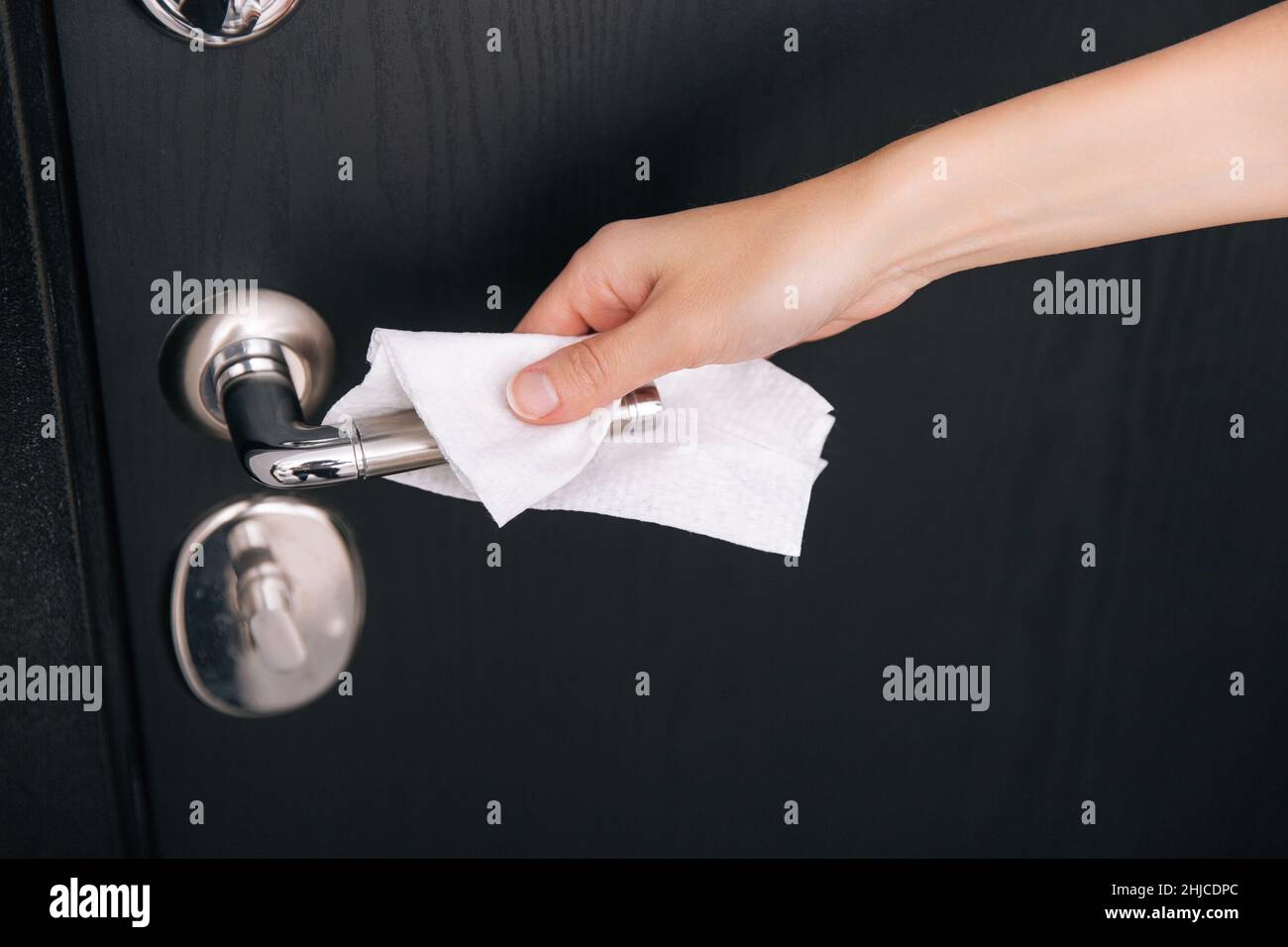 Cleaning black door handles with an antiseptic wet wipe. Woman hand using towel for cleaning home room door link. Sanitize surfaces prevention in Stock Photo