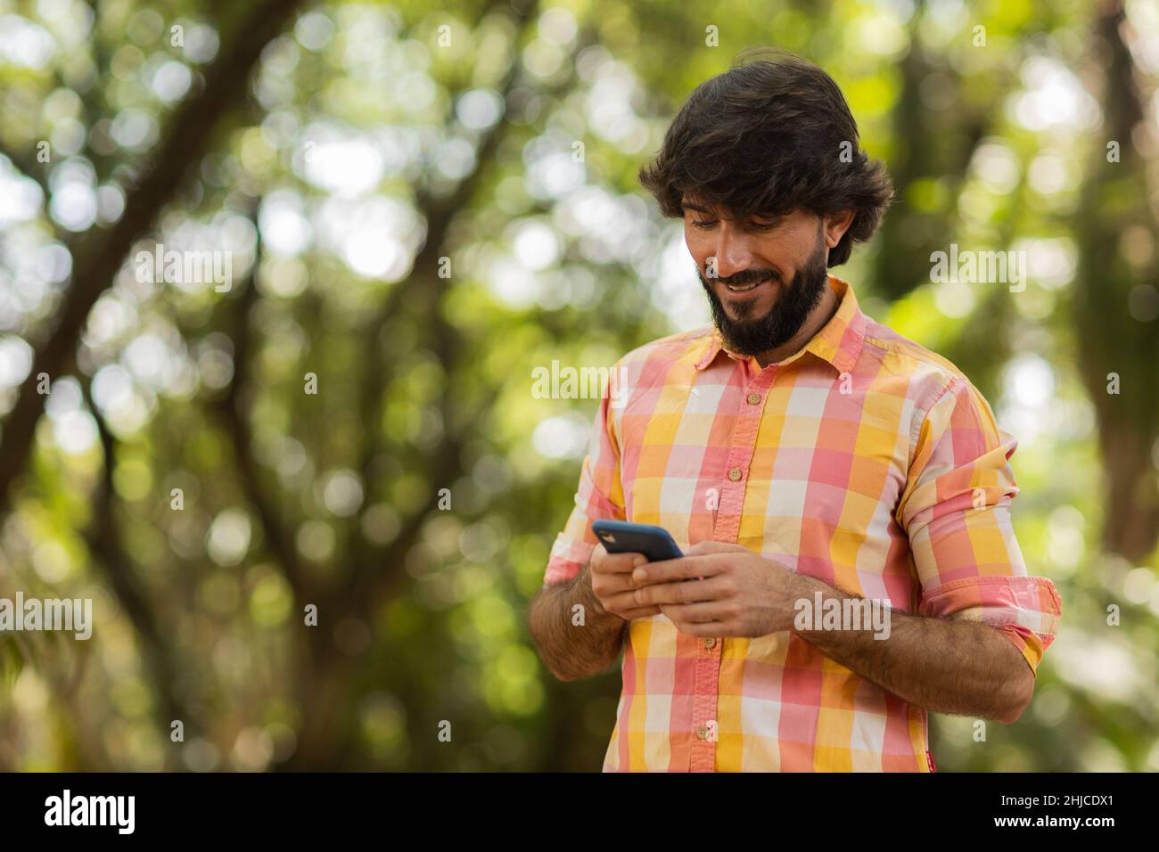 View of young man using a smartphone at day time with a green park in ...