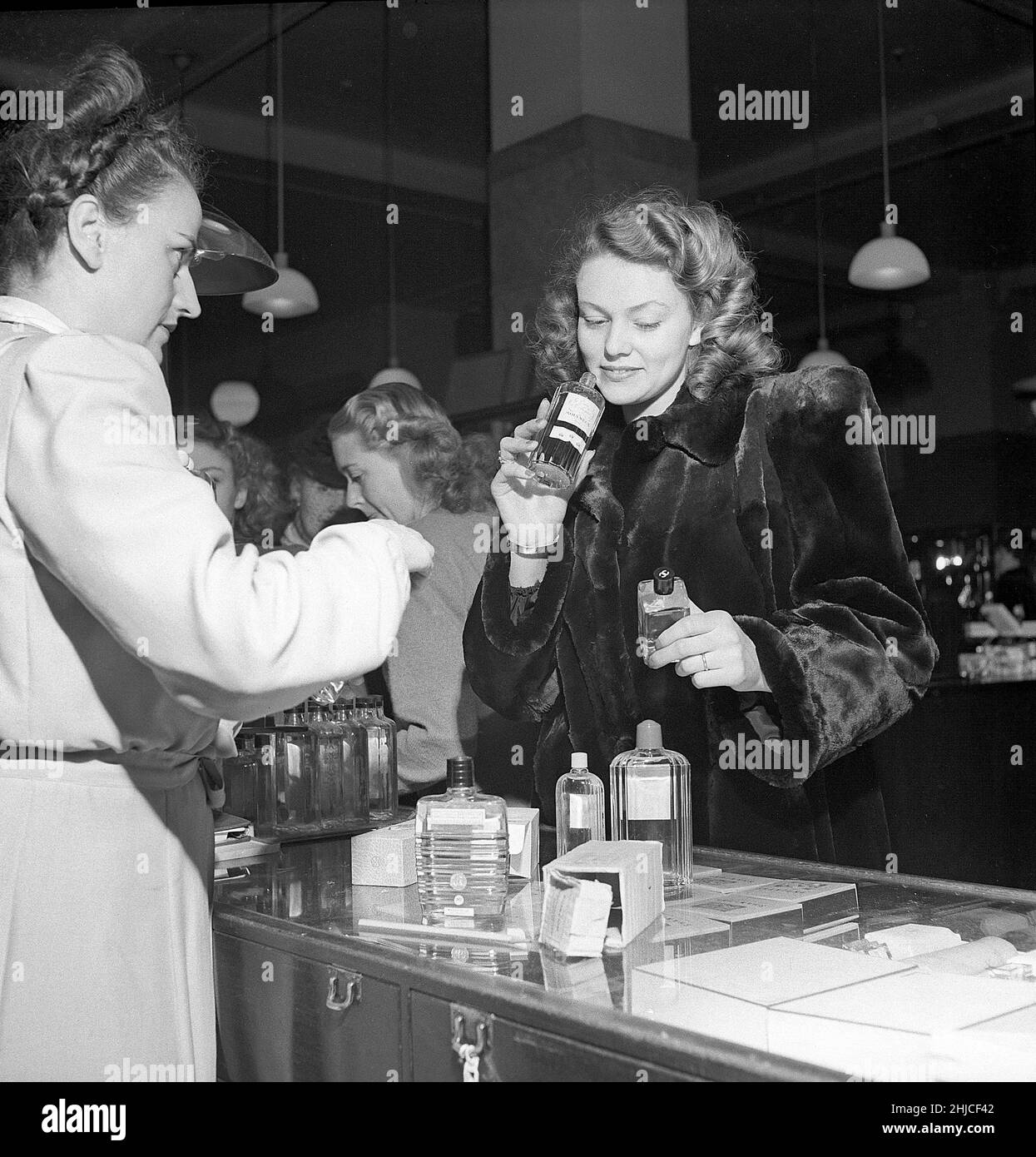 Shopping in the 1940s. A young woman in a perfume store where a sales woman is presenting some of the stores selection of cosmetics and perfumes. On the sales counter products from Peggy Sage is visible. She is Haide Göransson that 1949 was the symbol for the swedish ideal girl and featured on the cover of the magazine Life. She was described having a well-scrubbed Swedish look that was achieved only with soap and water. She was at this time the symbol of the natural look of the nordic women. Sweden 1947 Kristoffersson ref Y71-2 Stock Photo