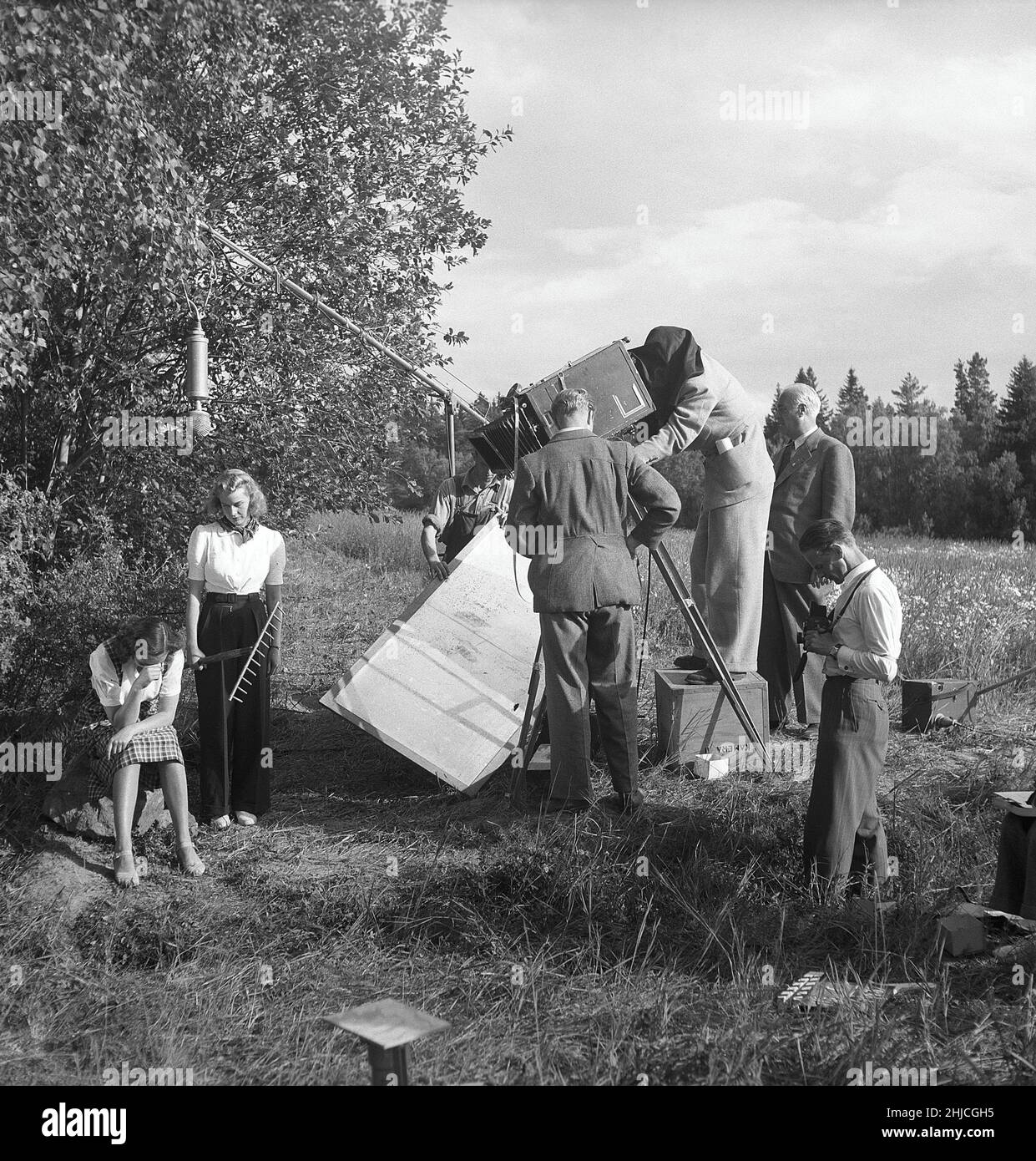 Filming in the 1940s. Filmcrew on set of the movie Ungt blod and actresses Brita Holmberg and Agneta Lagerfelt in an outdoor scene. To the right filmdirector Ivar Johansson. Filmphotographer has covered the part of the filmcamera where he sees the scene because of the intense sunlight his name is Karl-Erik Alberts. Place is Sturehov in the south of Stockholm. Sweden 1943 Kristoffersson ref E82-6 Stock Photo