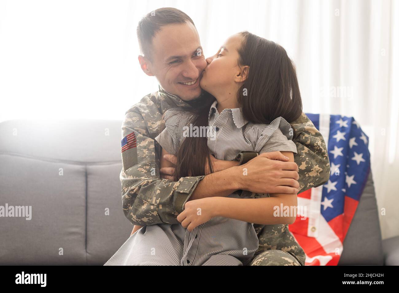 Happy little girl daughter with American flag hugging father in military uniform came back from US army, male soldier reunited with family at home Stock Photo