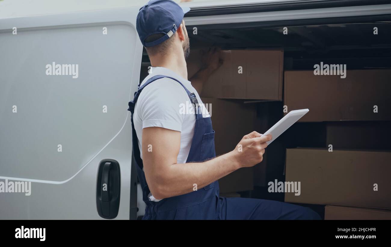 Delivery man holding digital tablet near cardboard packages in car ...