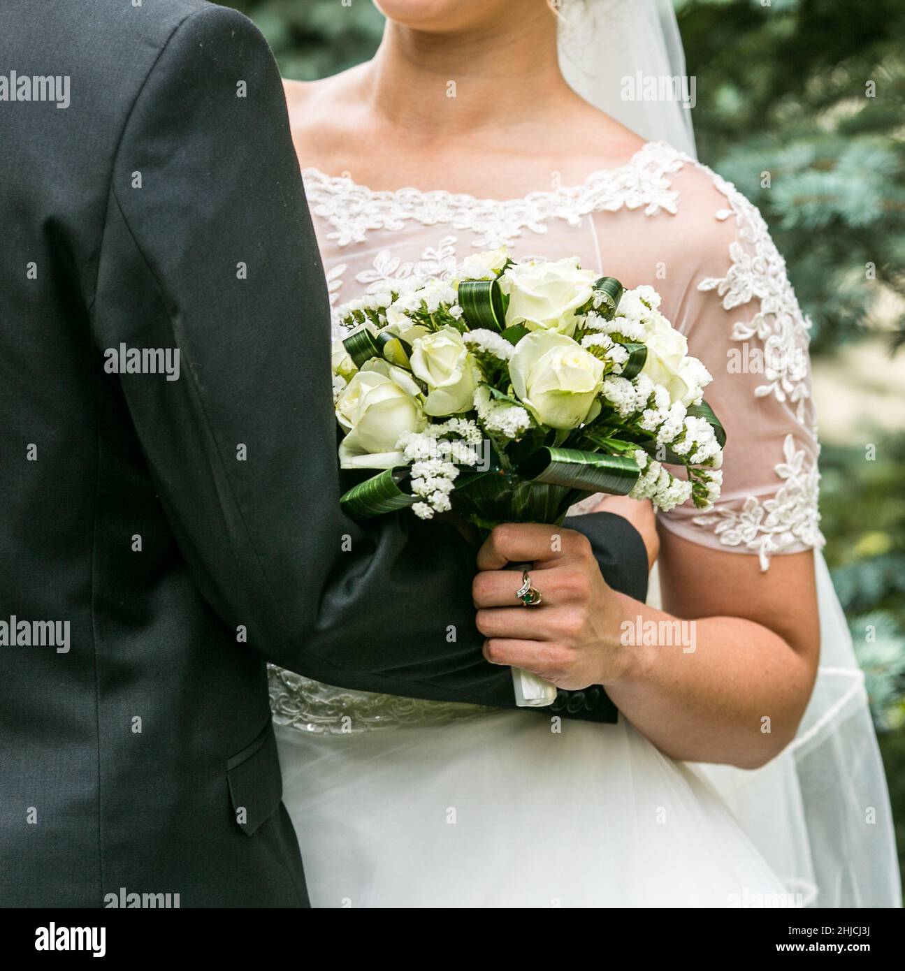 The bride and groom stand side by side and hold a wedding bouquet. Husband and wife hold flowers on their wedding day. Stock Photo