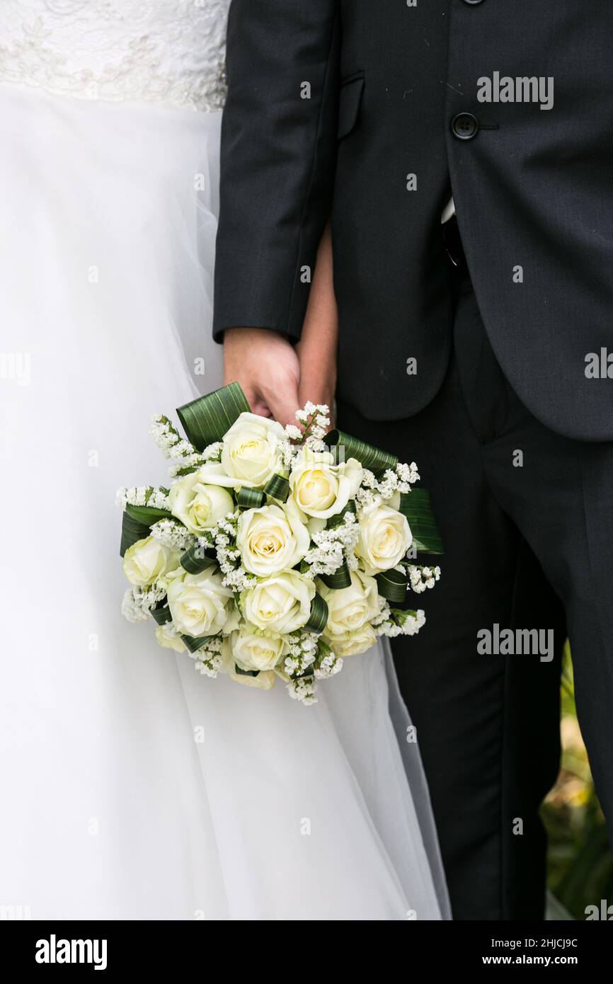 The bride and groom stand side by side and hold a wedding bouquet. Husband and wife hold flowers on their wedding day. Stock Photo