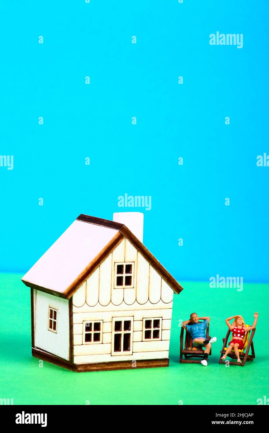 Conceptual image of a miniature figure couple sat in deckchairs at the side of a model house Stock Photo