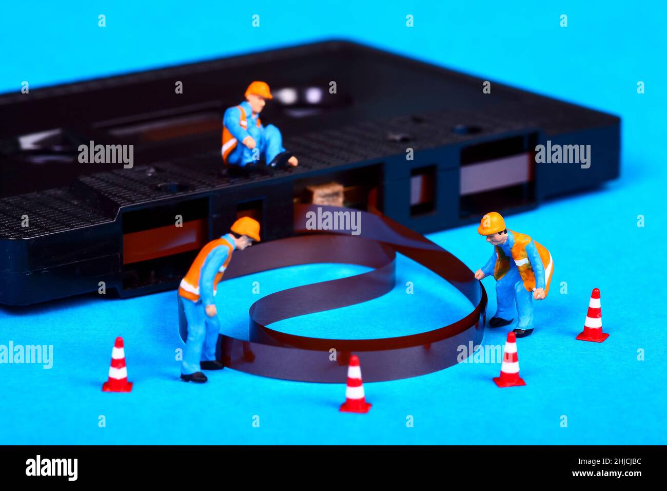 Conceptual image of miniature figure workmen inspecting an old vintage retro cassette tape that has unravelled after a tape jam Stock Photo