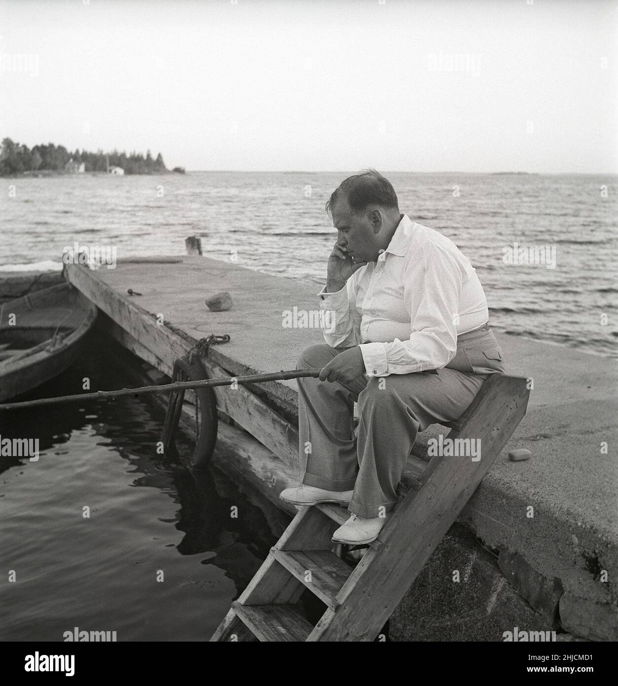 Fishing in the 1940s. A man is sitting by the lake fishing with a rod looking a little bit disapointed that no fish seems to catch. Sweden 1946 Kristoffersson ref V24-4 Stock Photo
