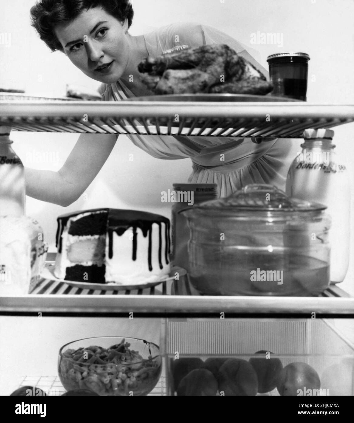 An American housewife gazes into her refrigerator, circa 1952. Stock Photo