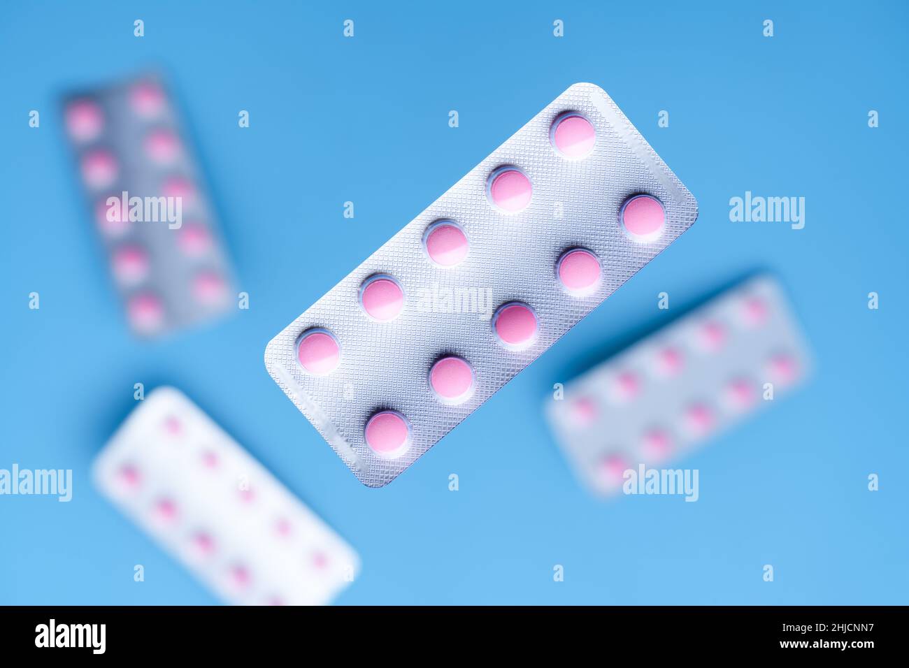 Flying pink pills in a blister pack on blue background. Medicine and healthcare concept Stock Photo