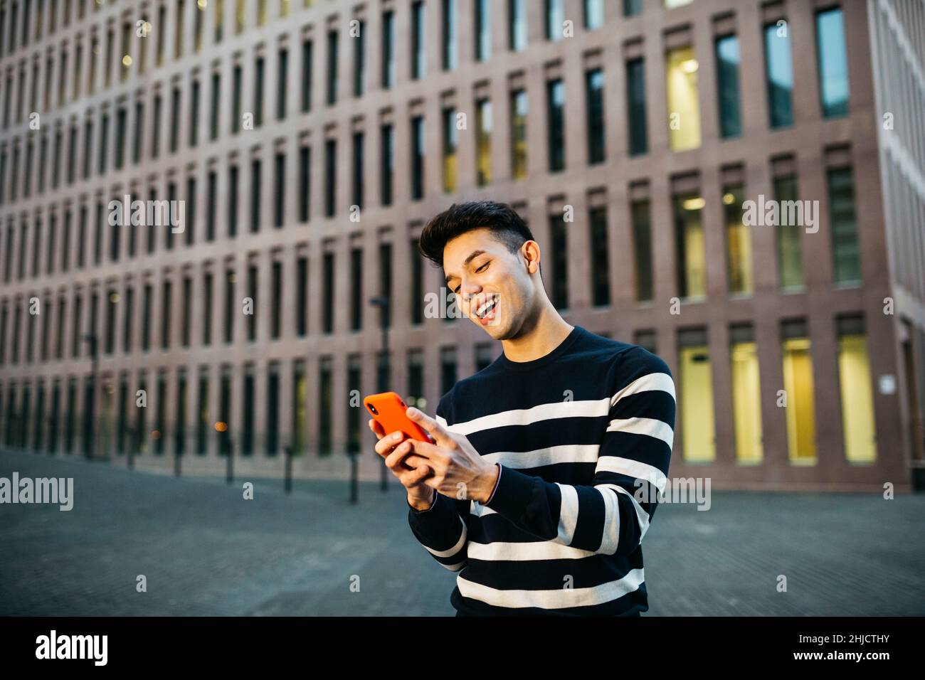 Young smiling man walking and using a red smartphone on street Stock ...