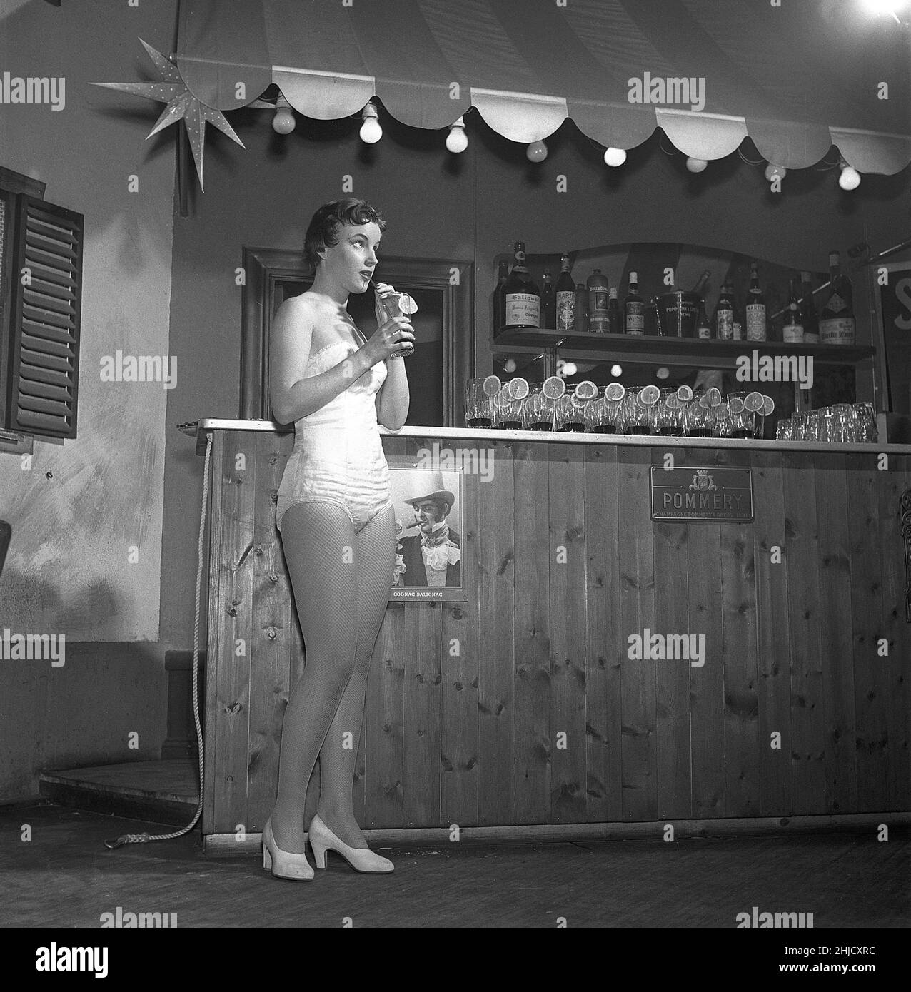 Woman in the 1950s. A young woman is standing in a bar with a drink in her hand sipping it with a straw. She is wearing clothes that from the theate or a variety show. Sweden 1956. ref Kristoffersson BE78-2 Stock Photo