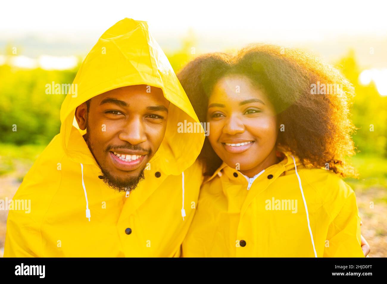 african american wife and husband in yellow raincoat with a hood feeling happy at sunset outdoors summer rain drop Stock Photo