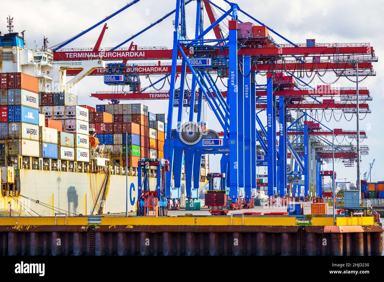 Ein Containerschiff wird tagsüber im Hamburger Hafen beladen; mit blau-rote Containerbrücken werden die Container an die richtige Position bugsiert Stock Photo