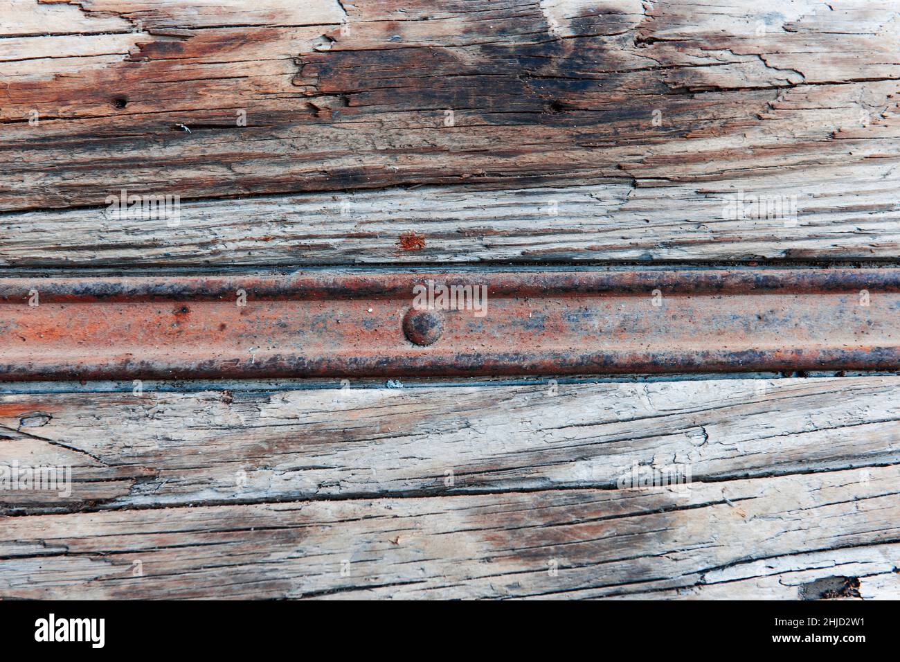 Full-frame view of a rusty metal rail in weathered wood. Stock Photo