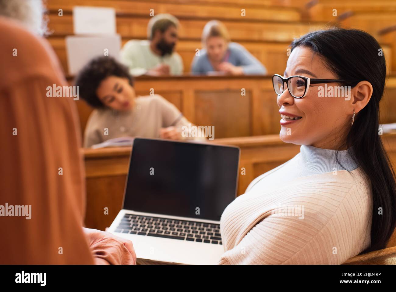 Smiling asian student holding laptop near teacher in university ...